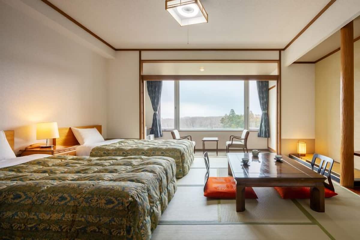 Ein Hotelzimmer mit zwei Betten, einem Esstisch, Stühlen, einem Fernseher und einem großen Fenster.
