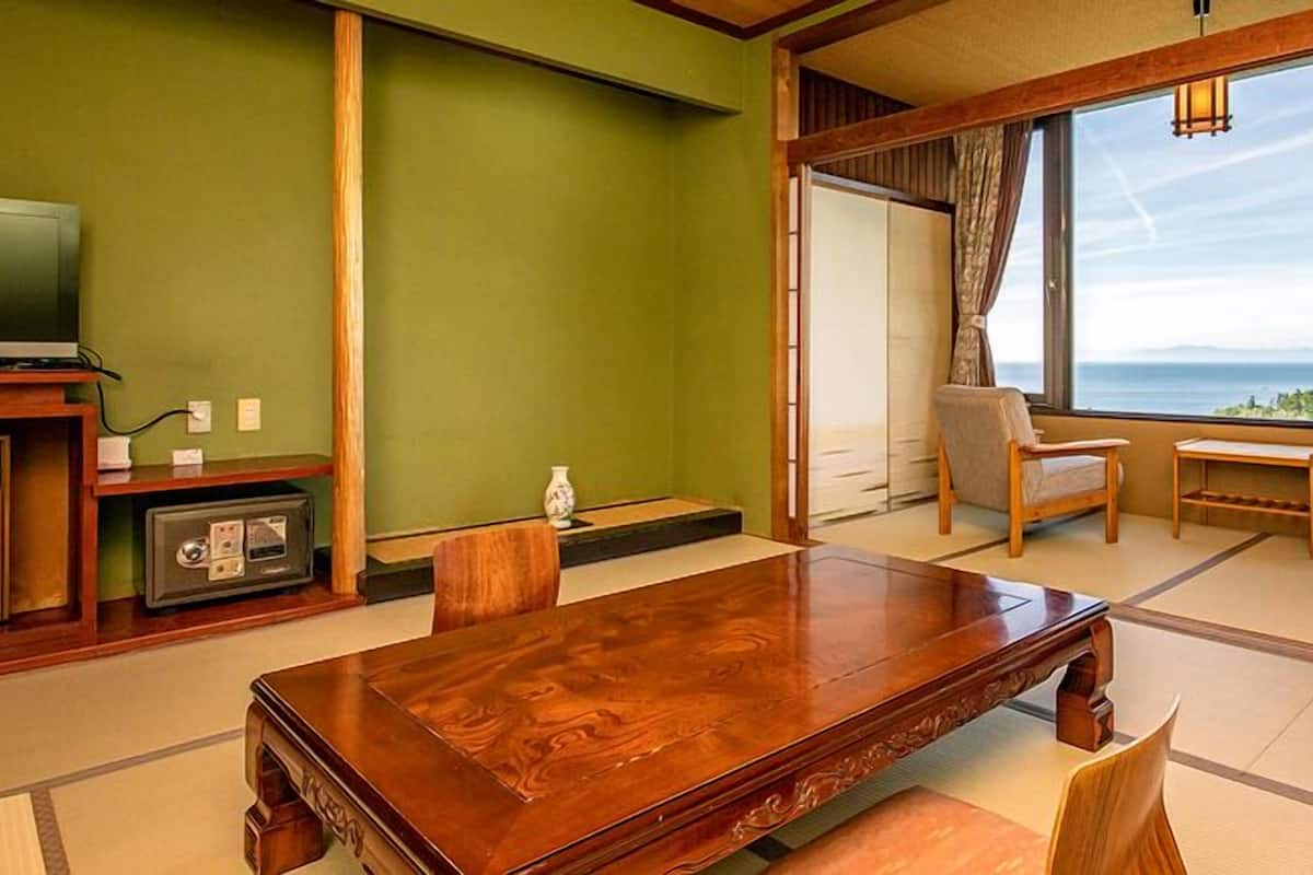 Ein traditioneller japanischer Raum mit Tatami-Böden, einem Holztisch, einem Fernseher und Meerblick.
