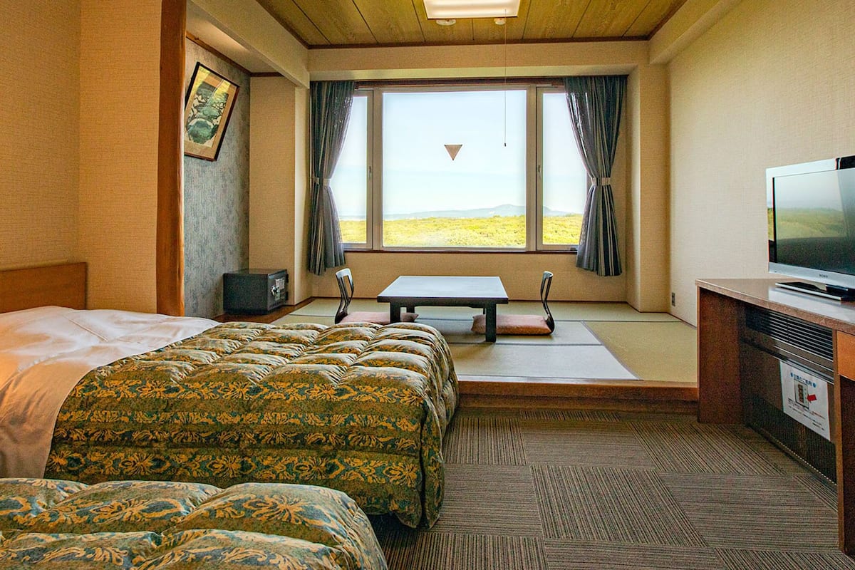 Ein Hotelzimmer mit Bett, Sofa, Fernseher, einem Fenster mit Vorhängen und Blick ins Freie.