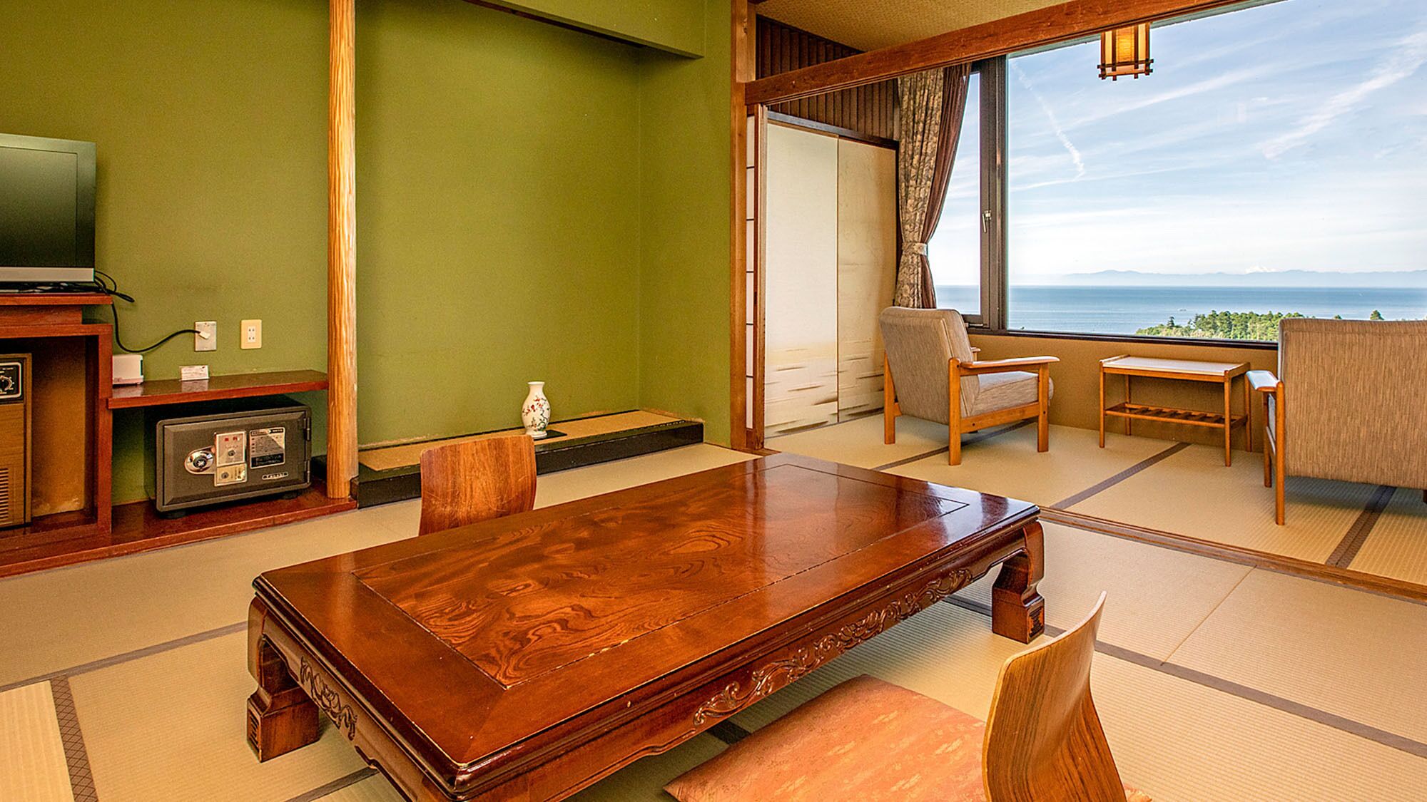 A traditional Japanese-style room with tatami flooring, a wooden dining table, a television, and a view of the sea.