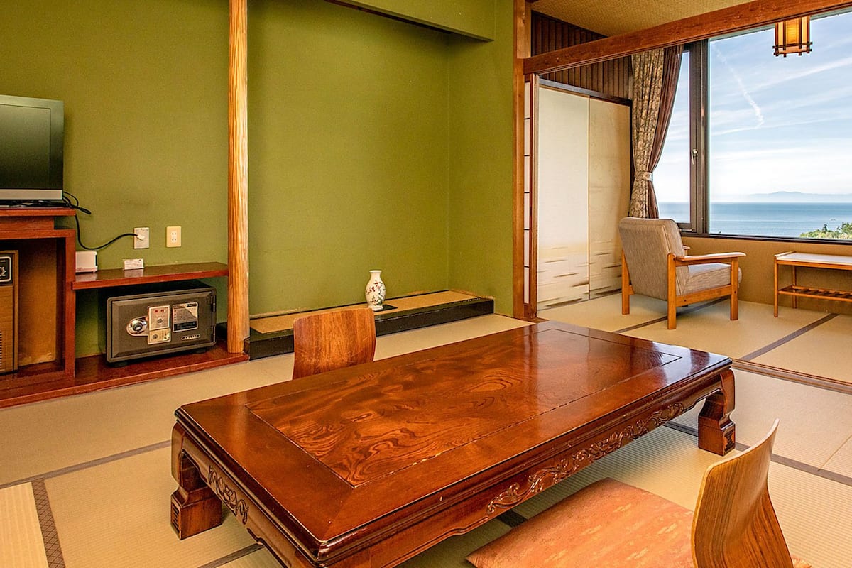 Ein traditioneller japanischer Raum mit Tatami-Bodenbelag, einem Holztisch, einem Fernseher und Blick auf das Meer.