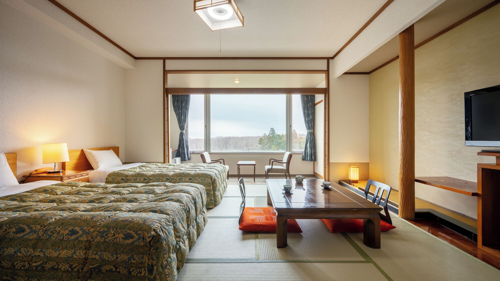 A hotel room with two beds, a dining table, chairs, a TV, and a large window.
