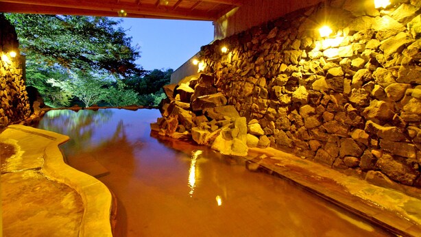 A stone-walled hot spring area with a curved pool and a wooden structure overhead.