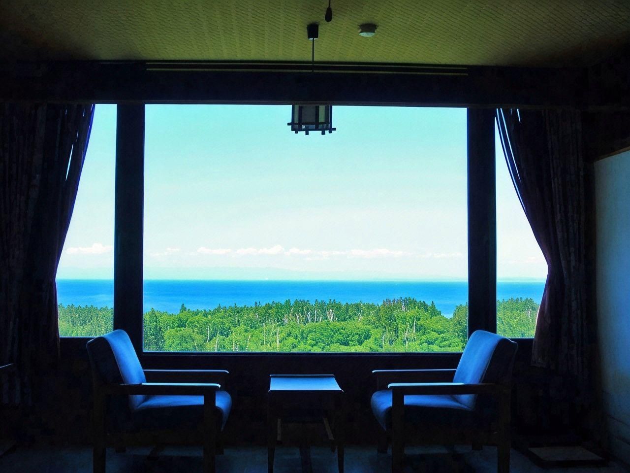 A room with two chairs facing a large window overlooking a forest and ocean.