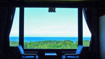 A room with two chairs facing a large window overlooking a forest and ocean.