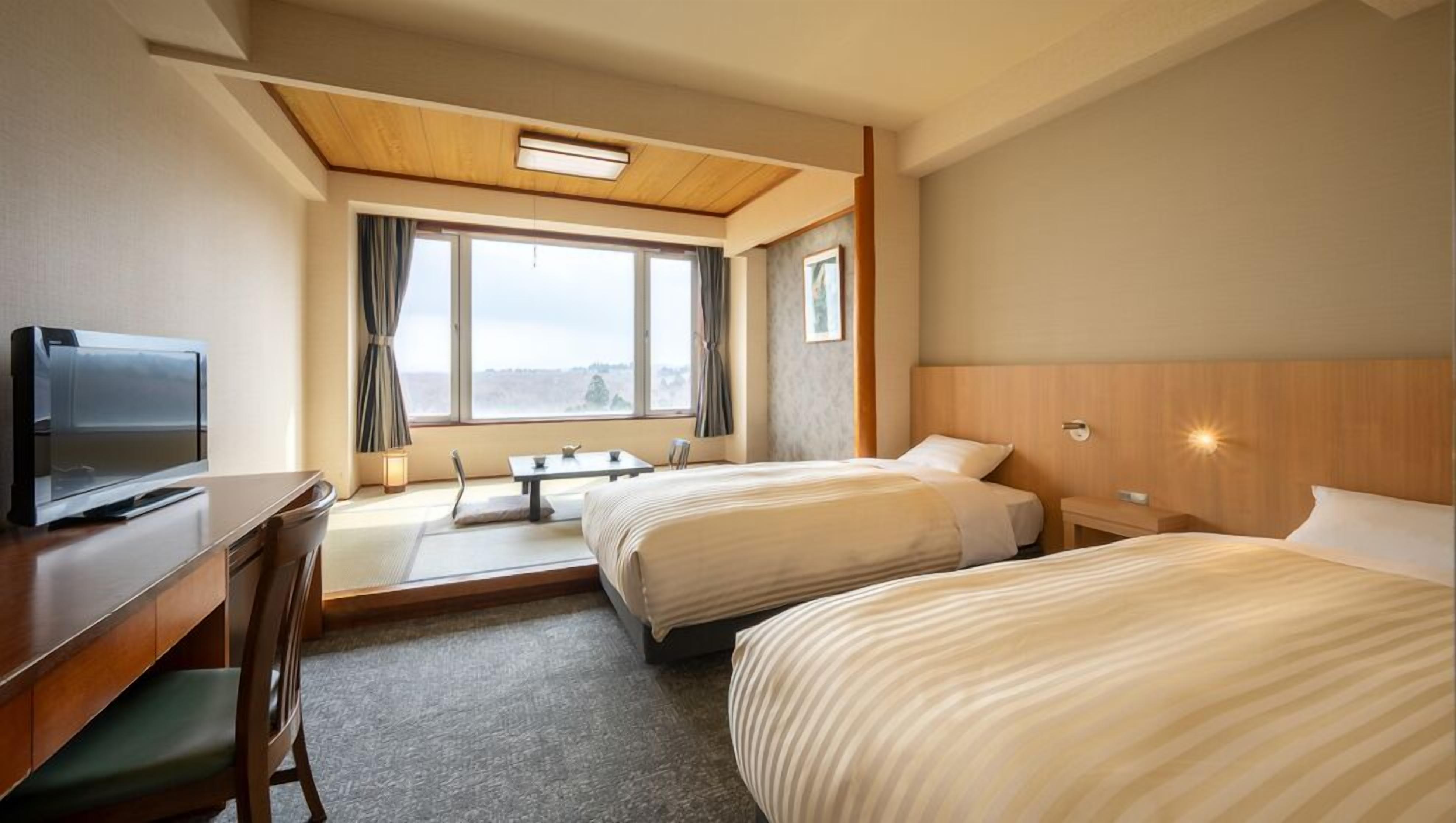 A hotel room with two beds, a desk with a TV, a small table, and a window with curtains.