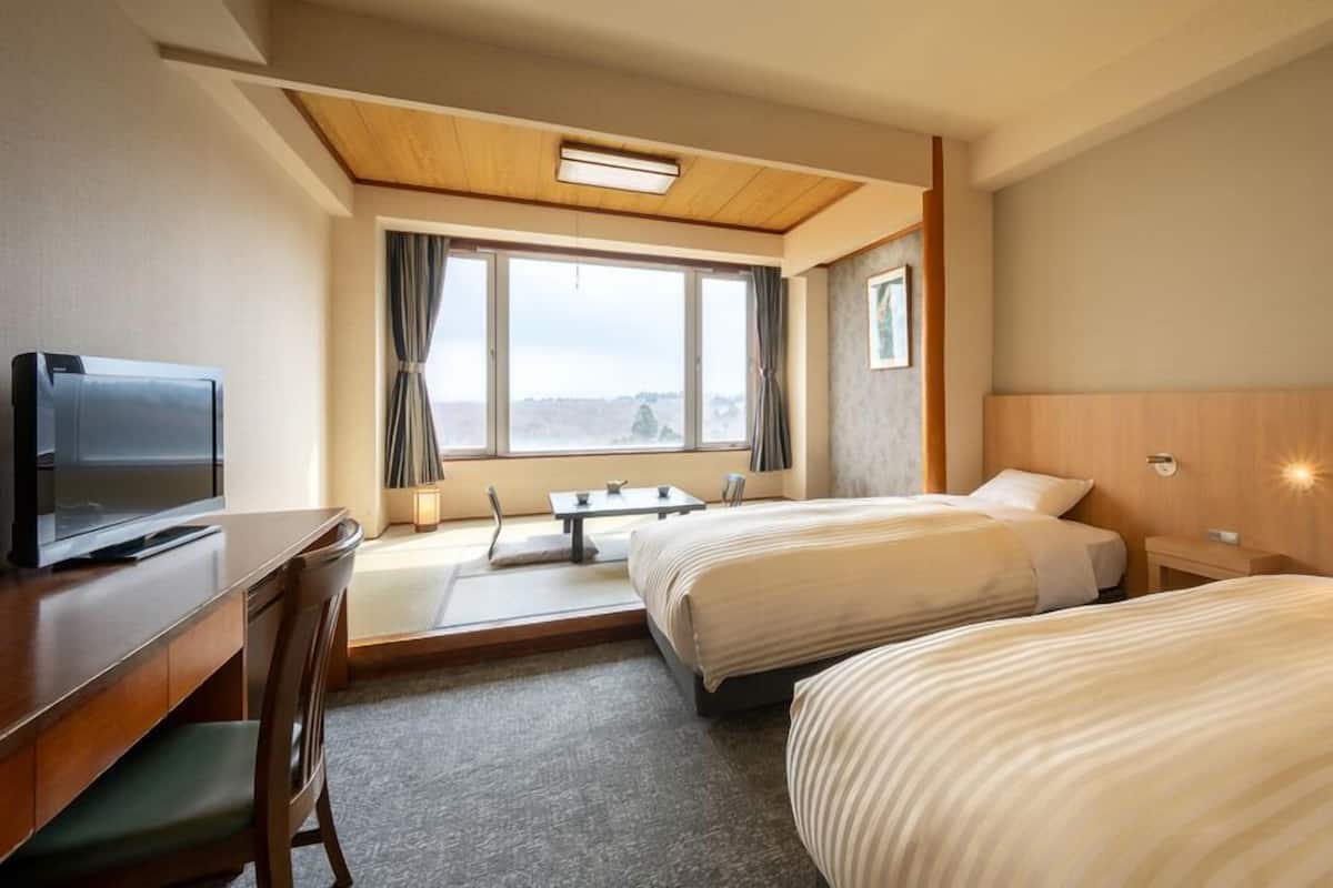 Ein Hotelzimmer mit zwei Betten, einem Schreibtisch mit Fernseher, einem kleinen Tisch und einem Fenster mit Vorhängen.