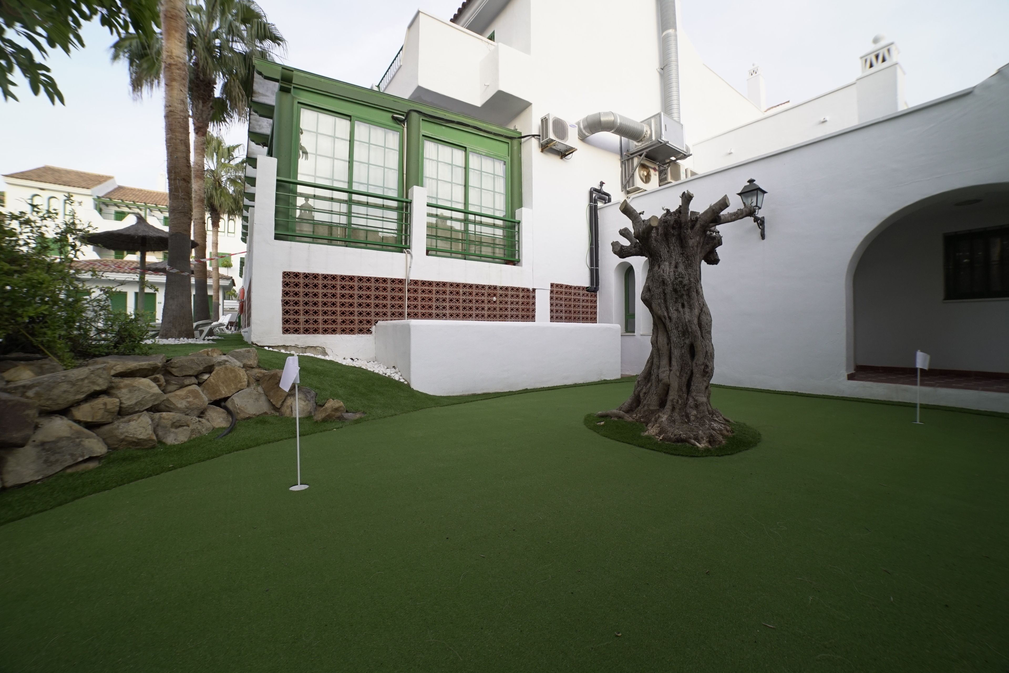 Um edifício com fachada branca, molduras de janela verdes e uma escultura de árvore em primeiro plano.