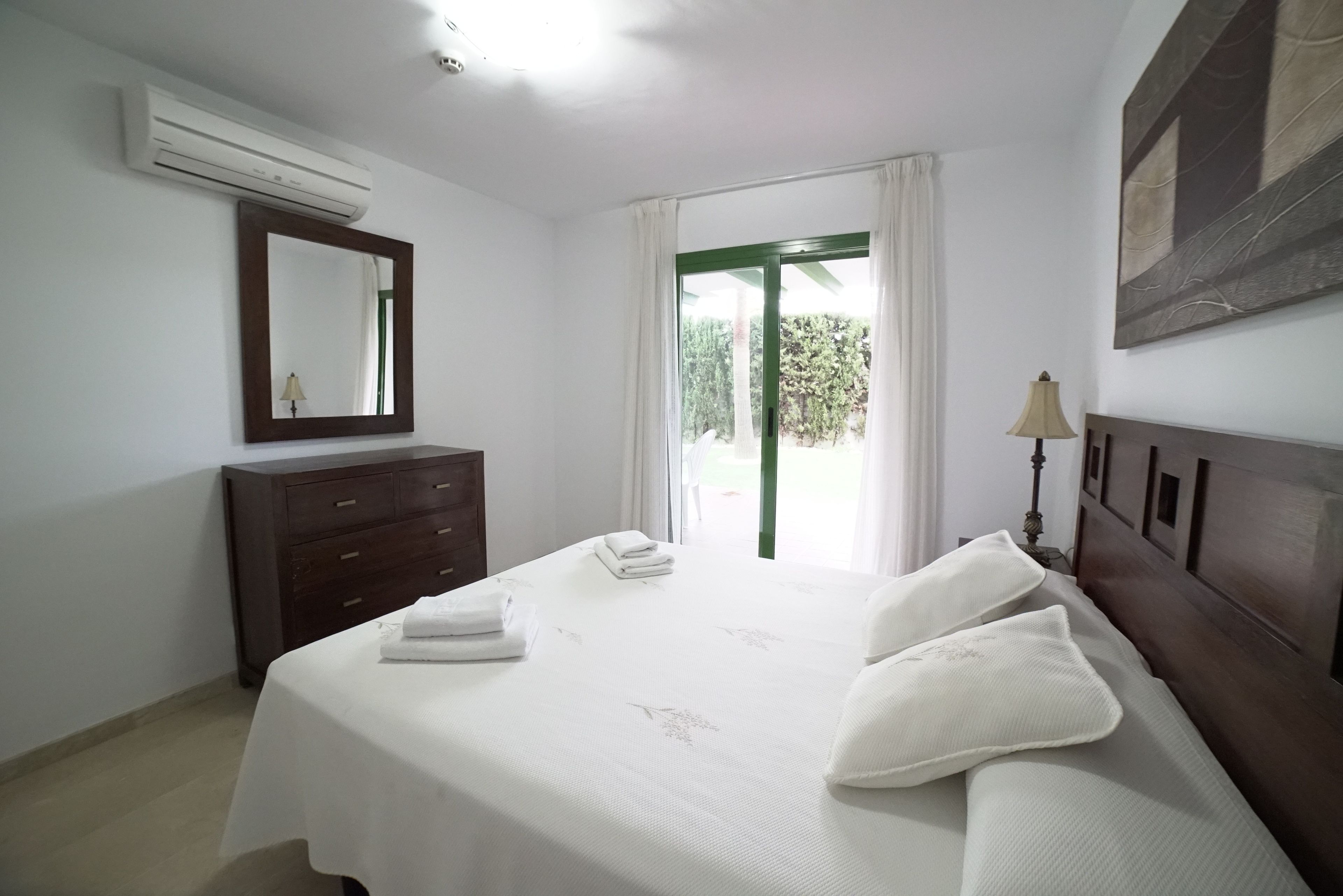 Habitación de hotel con cama, cómoda, espejo, ventana con cortinas y un cuadro en la pared.