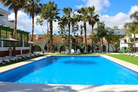 Una piscina al aire libre, sombrillas, sillones reclinables de piscina