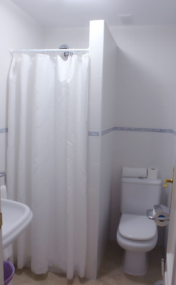Un baño con cortina de ducha blanca, inodoro y lavamanos.