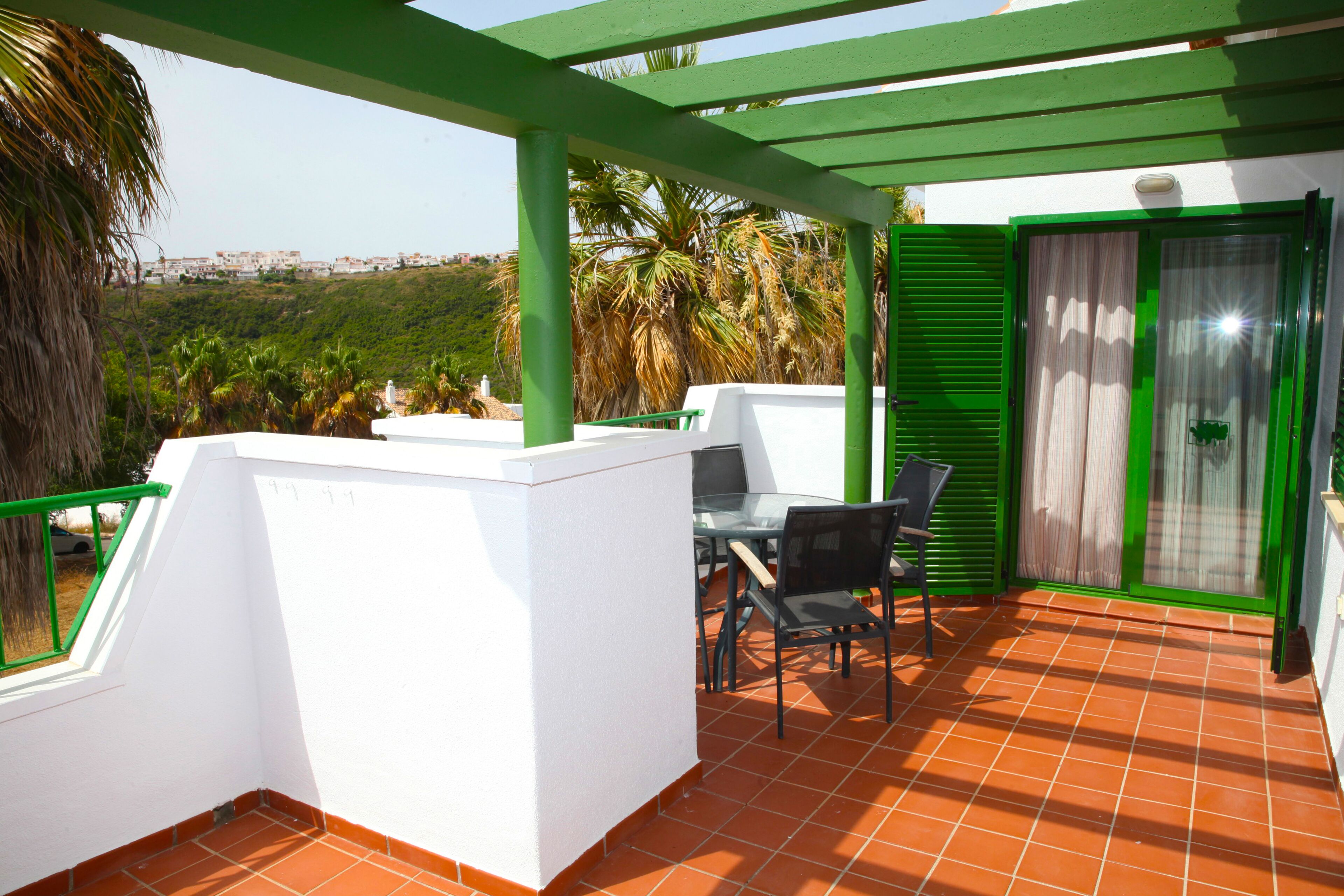 Eine Terrasse mit Tisch und Stühlen, eine grüne Pergola und ein Blick auf die Landschaft.