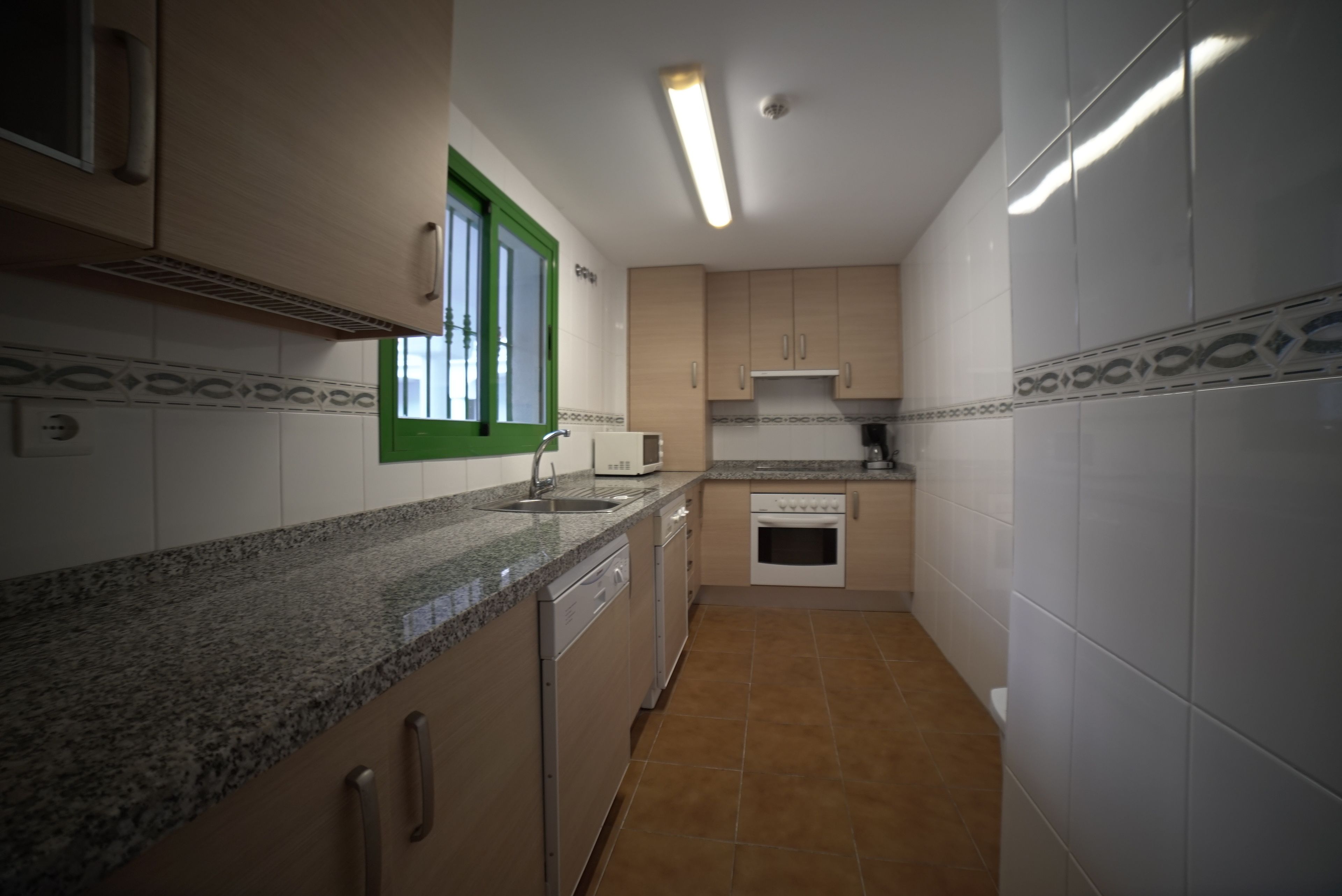 Una cocina compacta con encimera de granito, armarios blancos y una ventana con detalles verdes.
