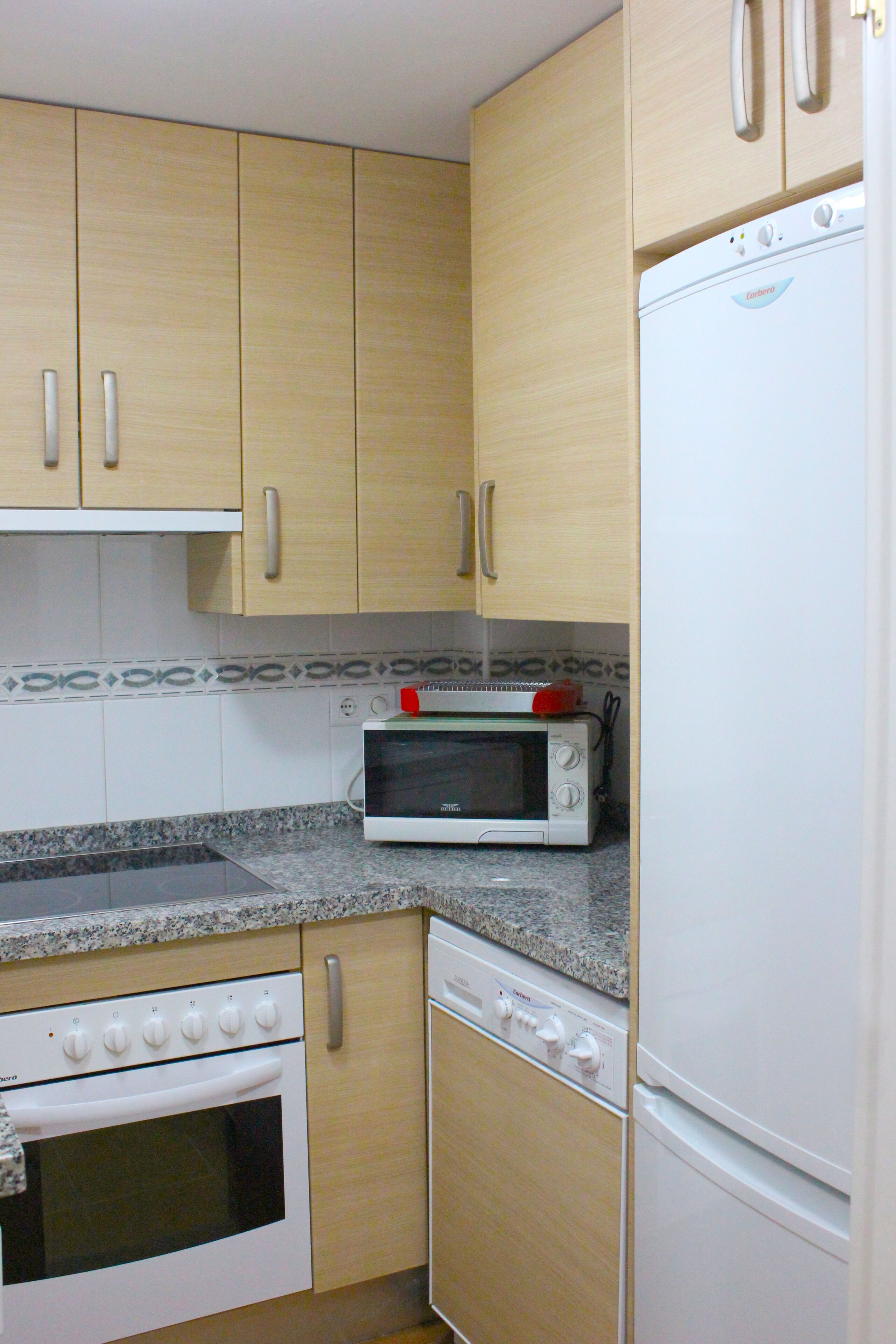 A kitchen with wooden cabinets, a built-in oven, a microwave, and a refrigerator.
