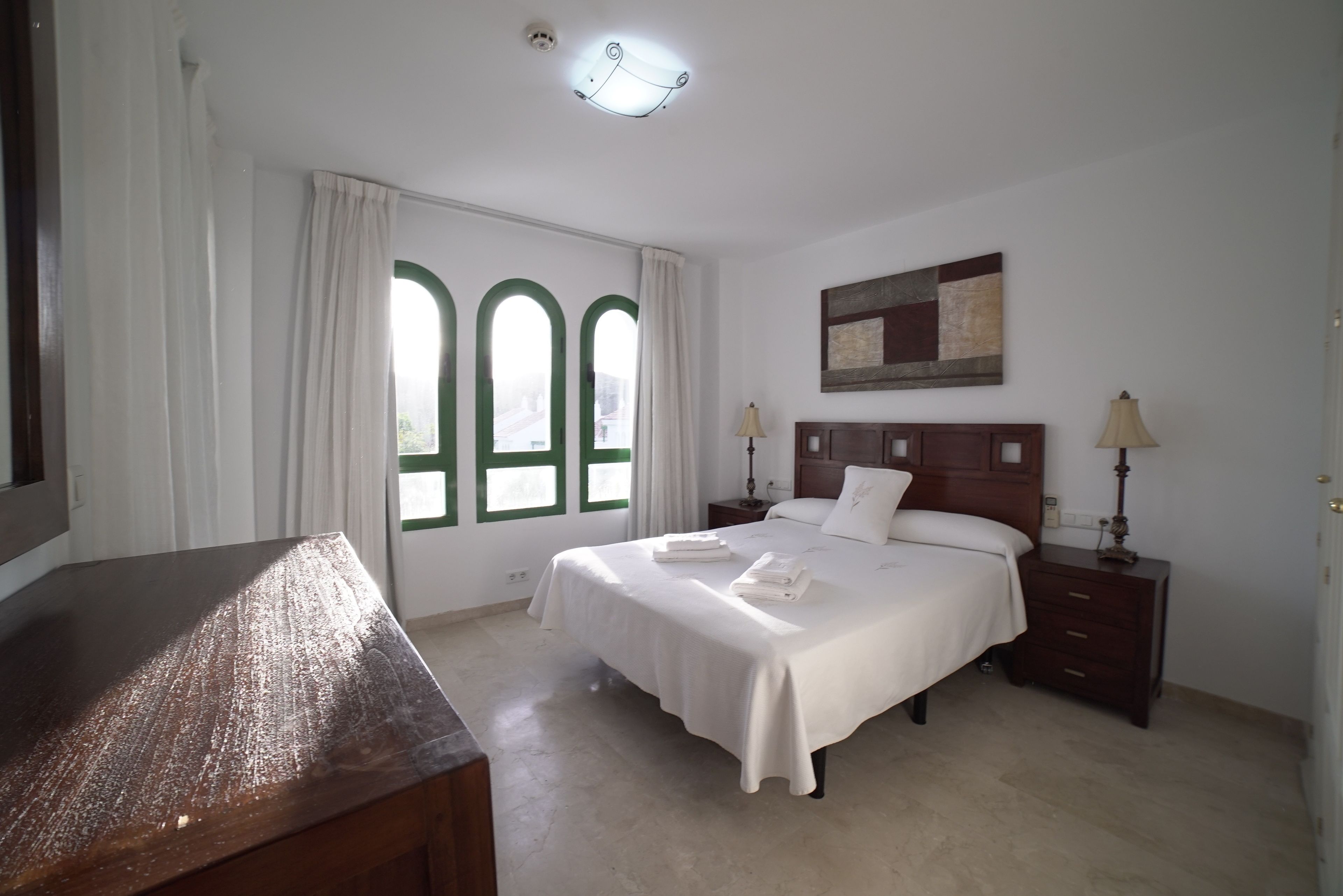 A hotel room with a bed, bedside tables, a desk, and a window with curtains.