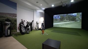 A room with artificial turf, golf bags, and a projection screen displaying a golf course.
