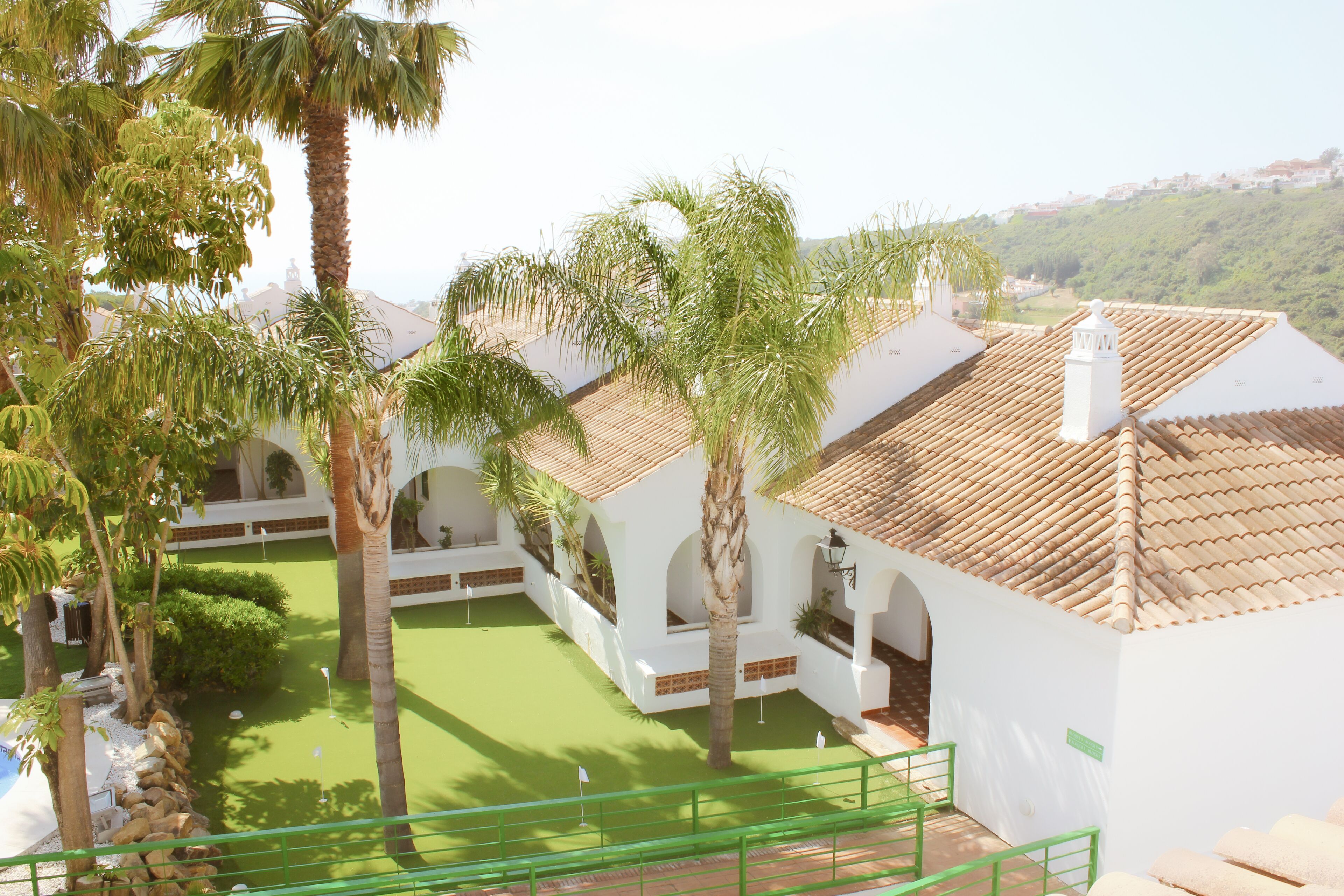 Un patio con edificios blancos, palmeras y un césped verde.