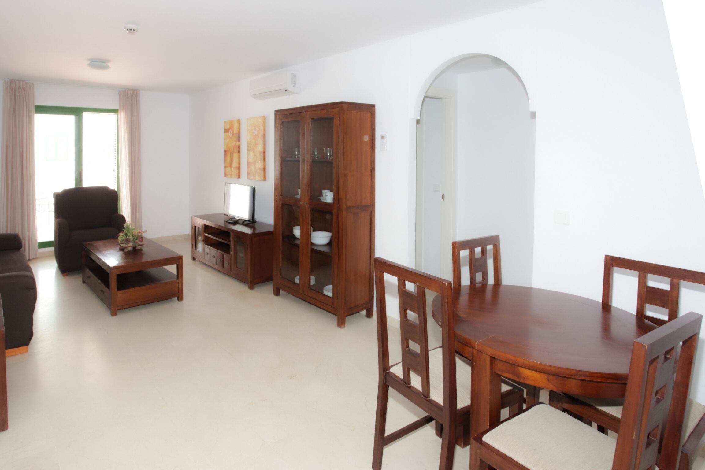 Una sala de estar con sofá, mesa de centro, mueble para televisión, aparador de madera y mesa de comedor con sillas.