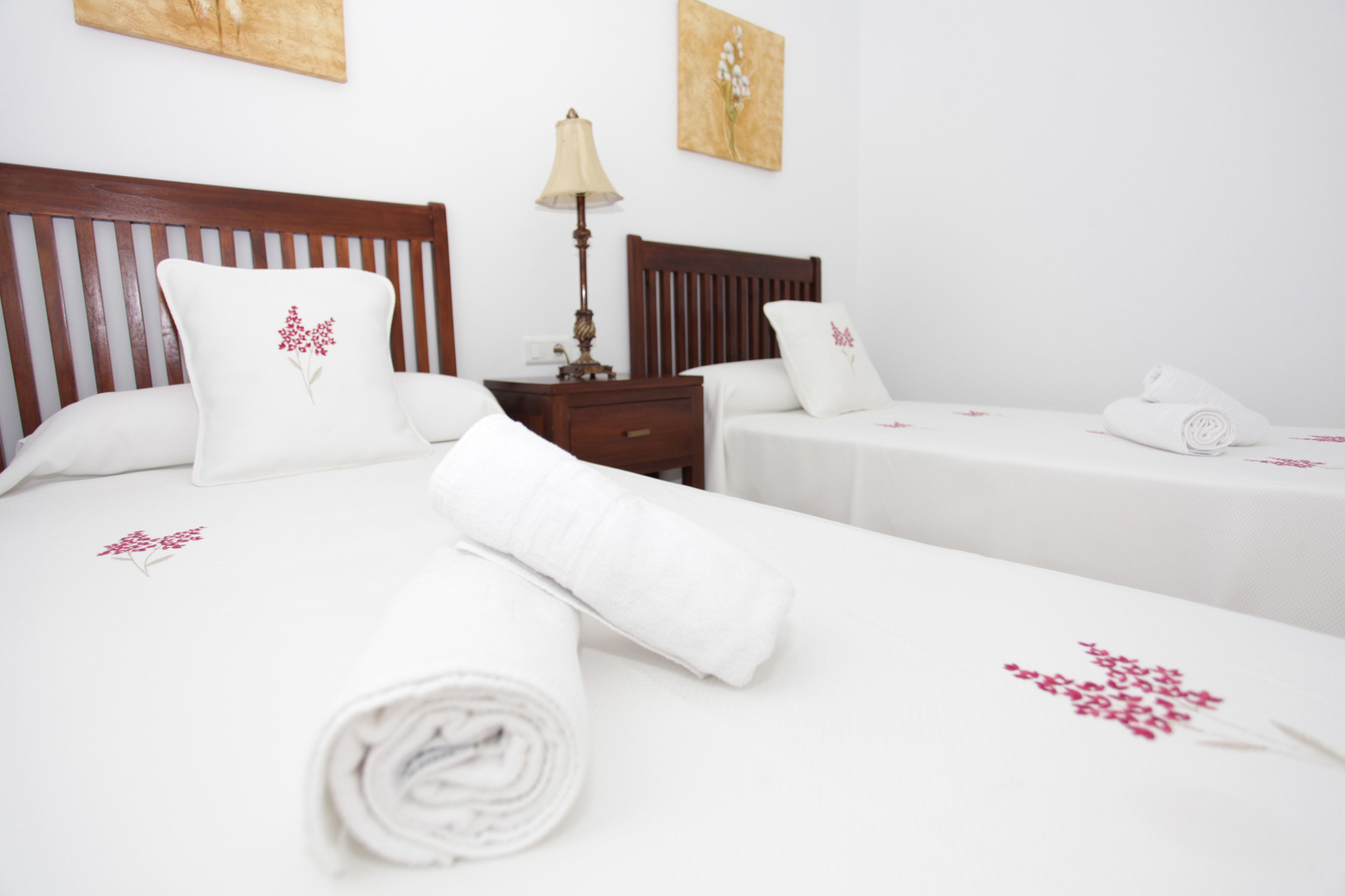 A hotel room with two beds, white linens, and floral pillows.