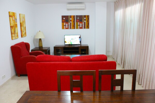 Una sala de estar con un sofá rojo, una mesa de madera y un televisor sobre un mueble.