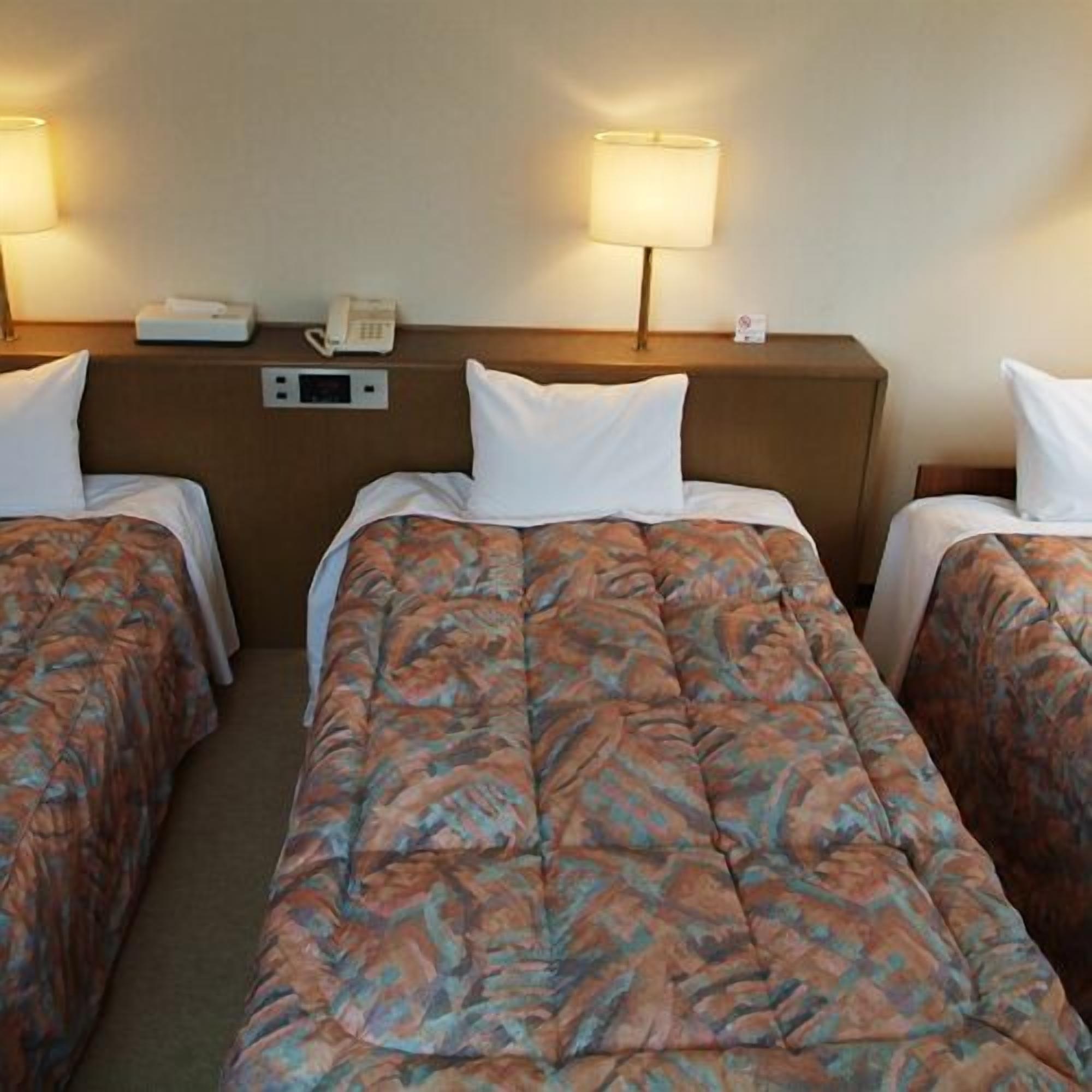 Ein Hotelzimmer mit zwei Betten, einem Nachttischtelefon und einem Nachttisch mit Lampe.