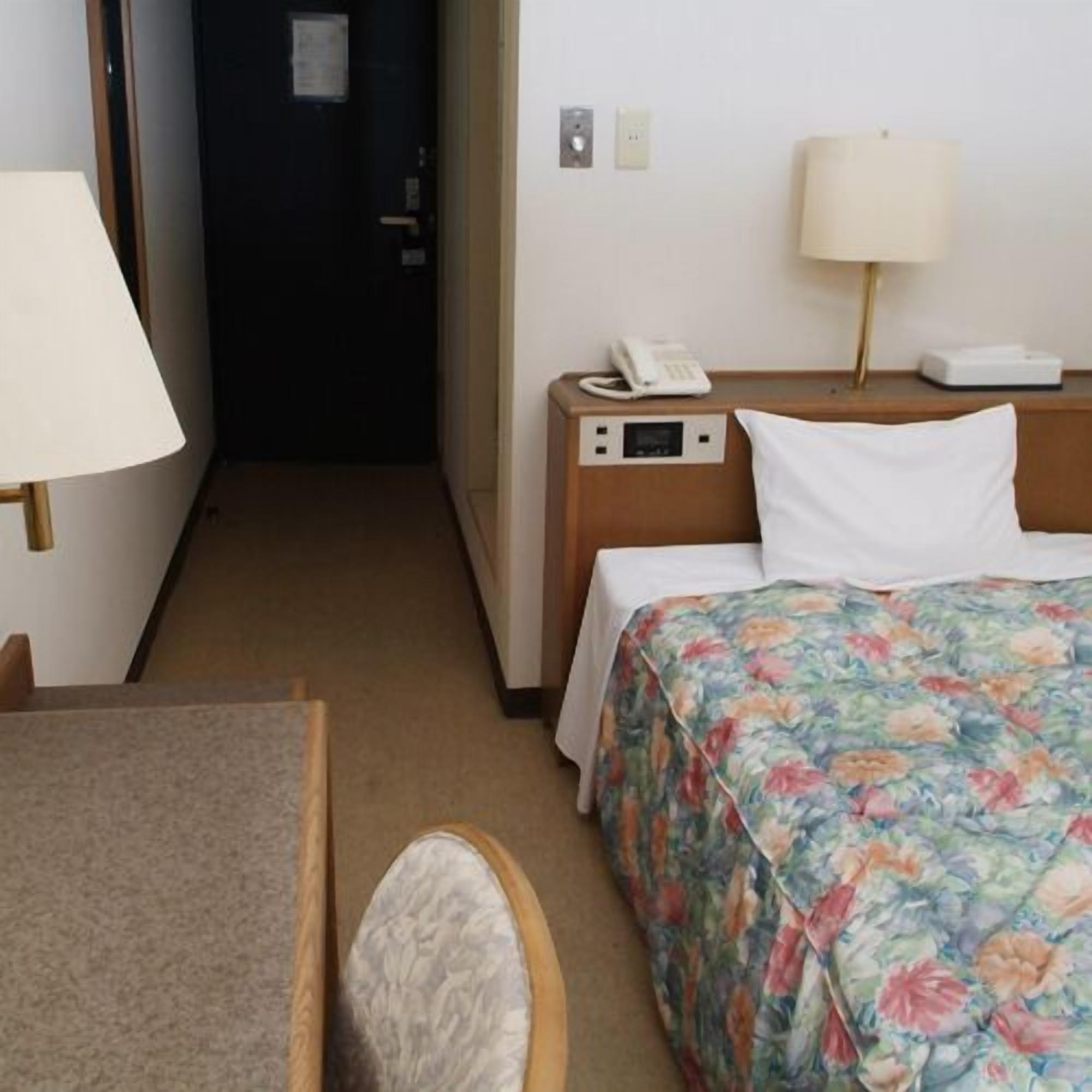 Ein Hotelzimmer mit einem Bett, einem Nachttisch mit Lampe, einem Telefon und einem kleinen Tisch mit Stuhl.