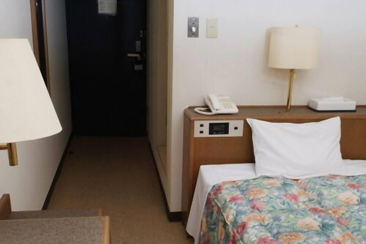 Habitación de hotel con cama, mesita de noche con lámpara, teléfono y una pequeña mesa con silla.