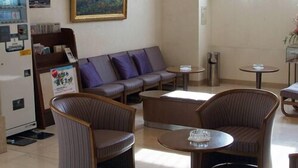 Um saguão de hotel com sofá, poltronas, mesa de centro, geladeira e um quadro na parede.