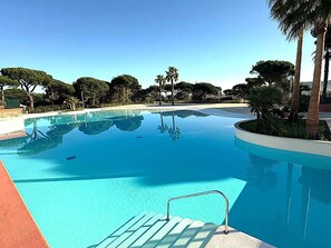 A clear blue swimming pool with a metal ladder, surrounded by palm trees and other greenery.