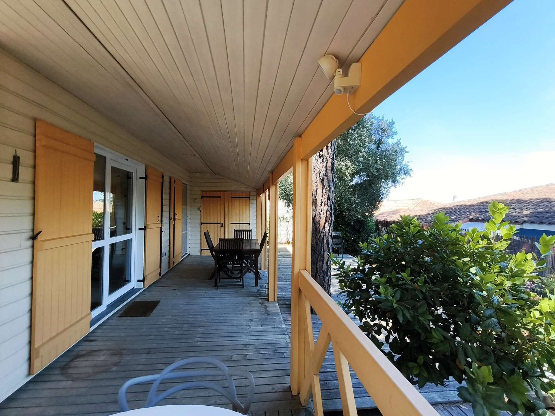 Un porche cubierto con una mesa y sillas, barandillas de madera y vistas al exterior.