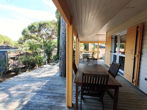 A wooden deck with a table and chairs, surrounded by a garden with various plants and trees.