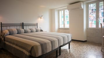 A bedroom with a bed, a nightstand, a wall-mounted lamp, and a window with a view of buildings.