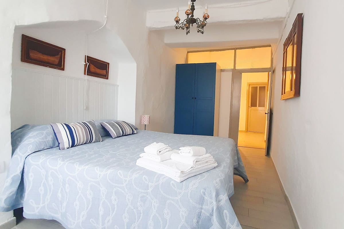Ein Schlafzimmer mit einem Bett, Kissen, einem gefalteten Handtuch, einem blauen Kleiderschrank und einer Tür zu einem anderen Raum.