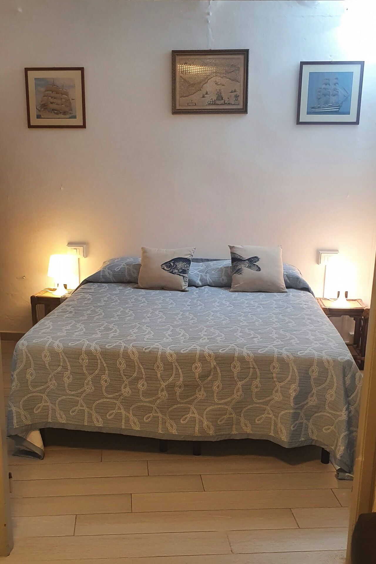 A bedroom with a bed, two bedside tables, and three framed pictures on the wall.