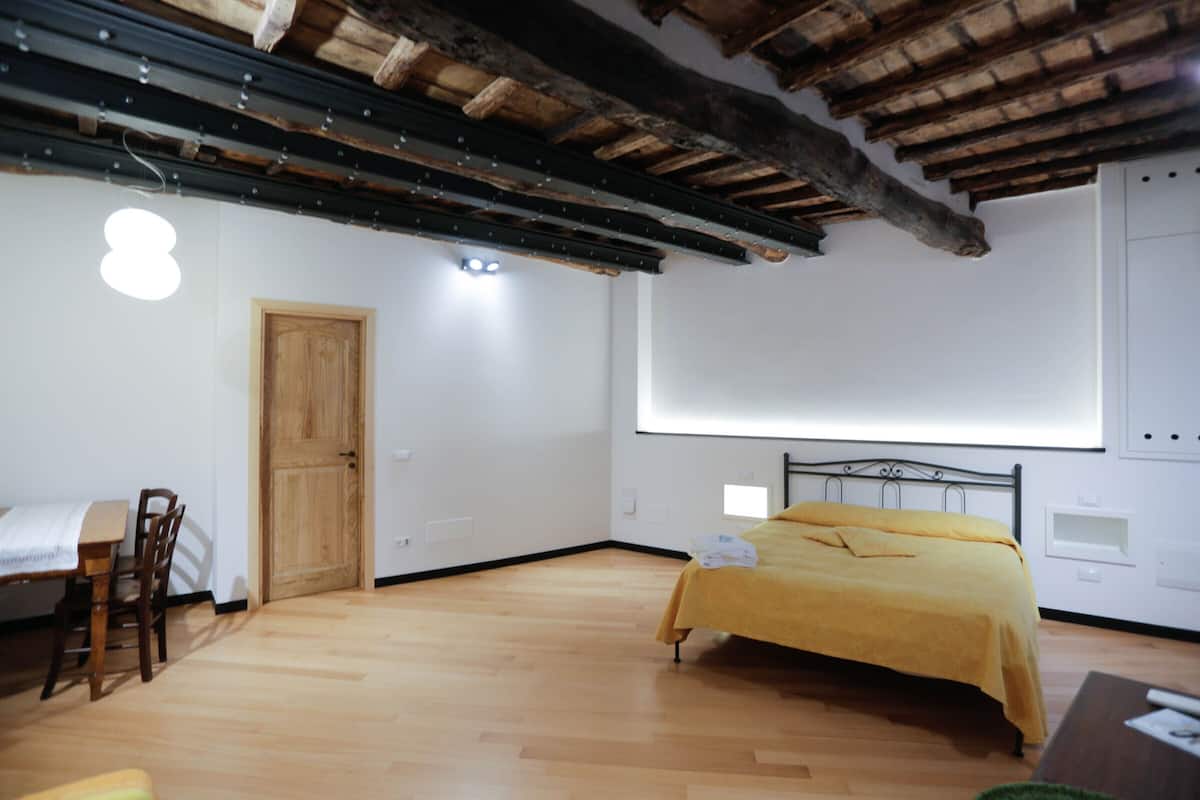 Ein Schlafzimmer mit Holzboden, einem Bett mit gelber Decke, einer Holztür und einer weißen Wand mit Projektionsschirm.