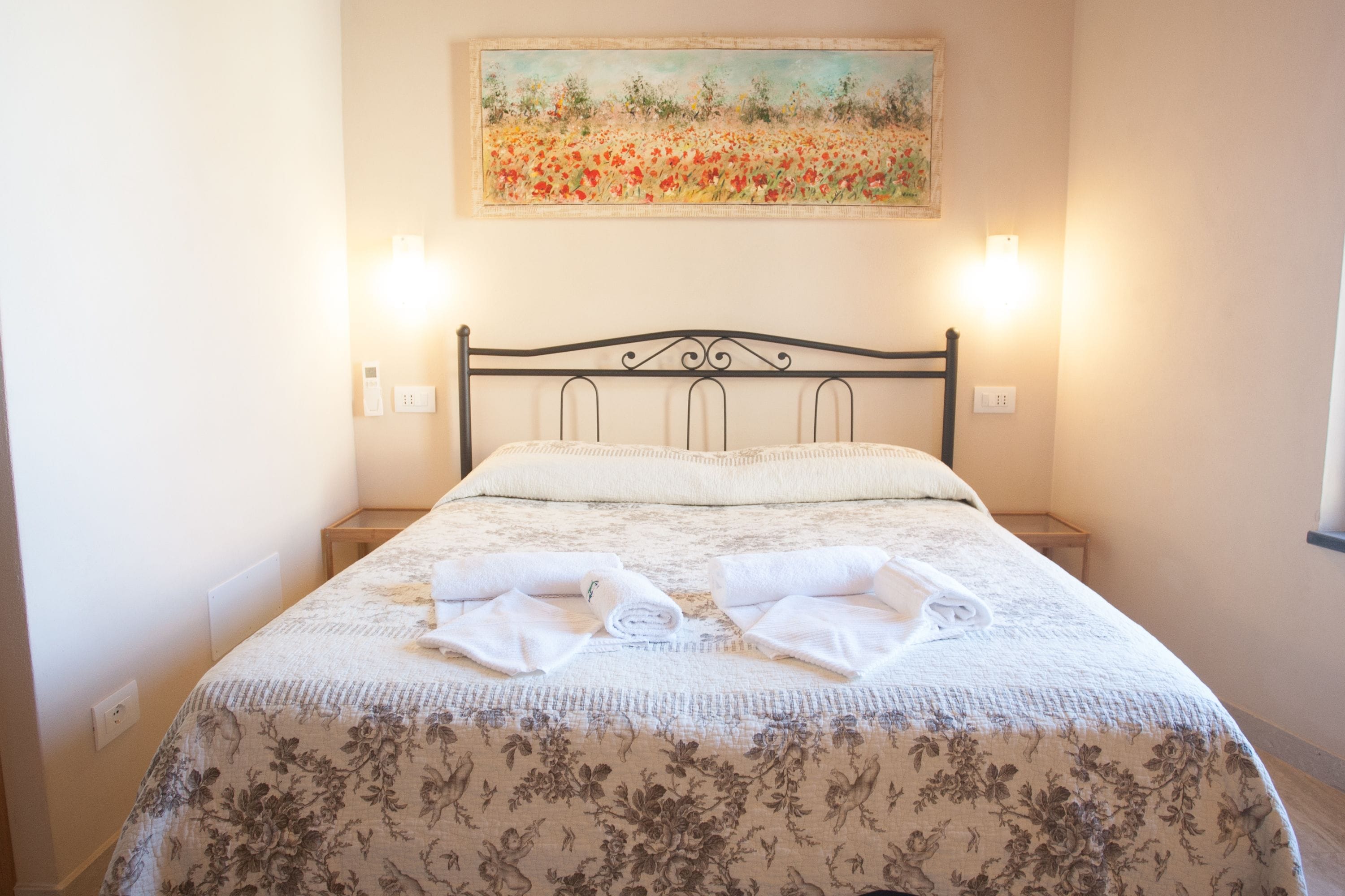 A neatly made bed with floral bedding, two bedside tables, and a painting above the bed.