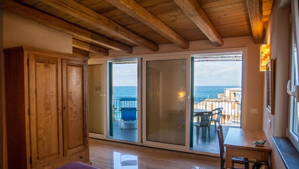 Una habitación con techo de madera, una cama con sábanas blancas, un armario de madera y vistas al mar a través de grandes puertas correderas de vidrio.