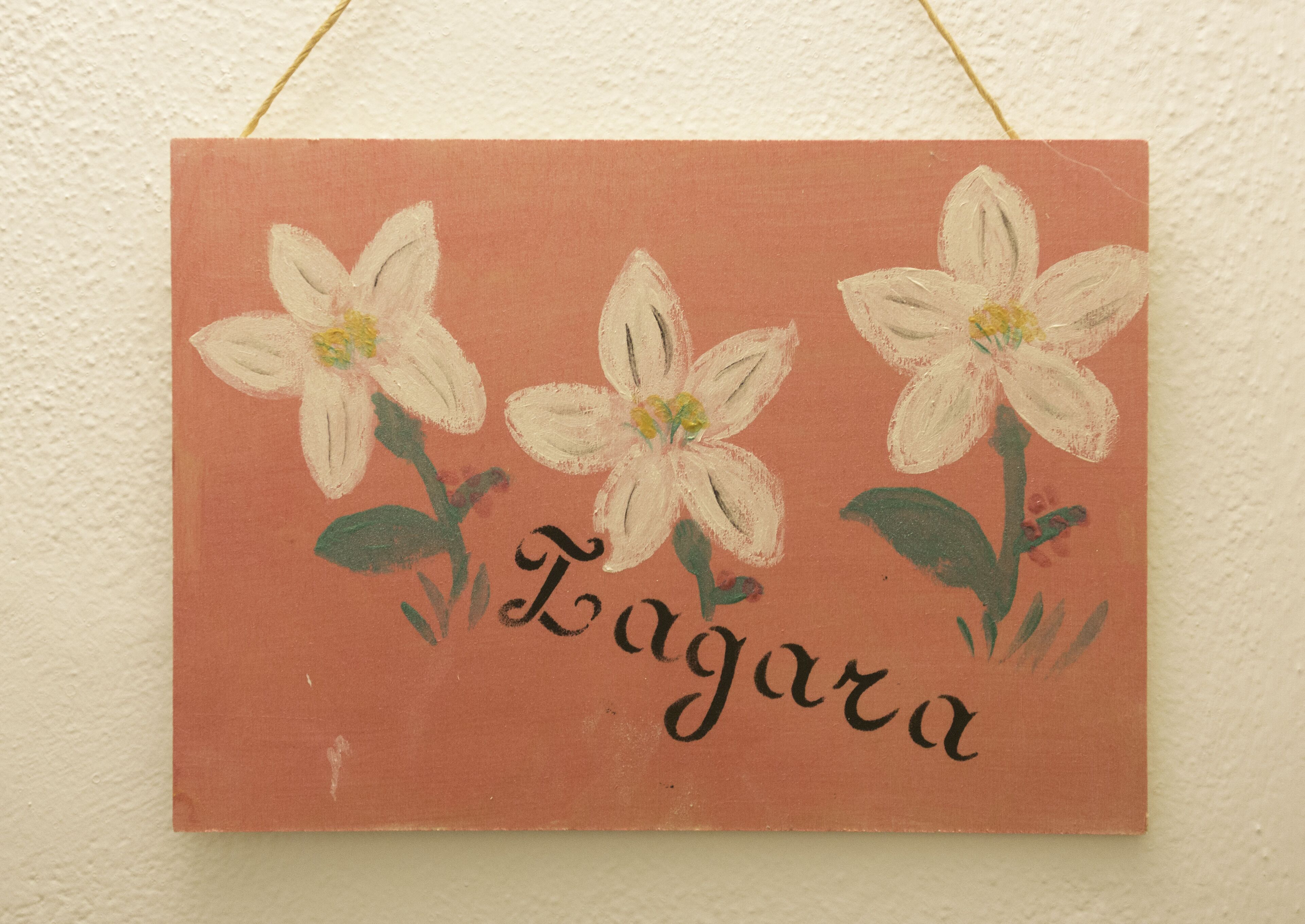 Ein Wandbehang mit drei weißen Blumen und dem Schriftzug "Laguna" auf beigem Hintergrund.