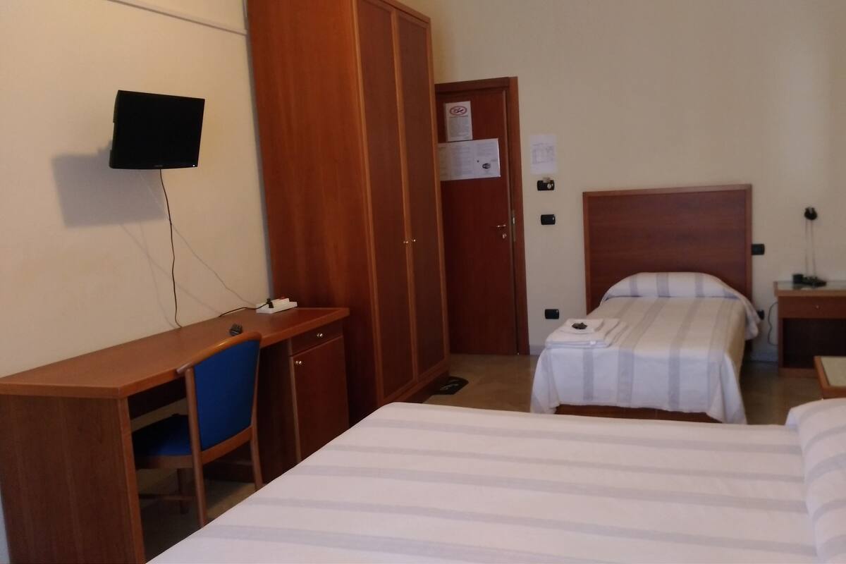 Ein Hotelzimmer mit Bett, Schreibtisch, Stuhl, Kleiderschrank, Fernseher und Nachttisch.