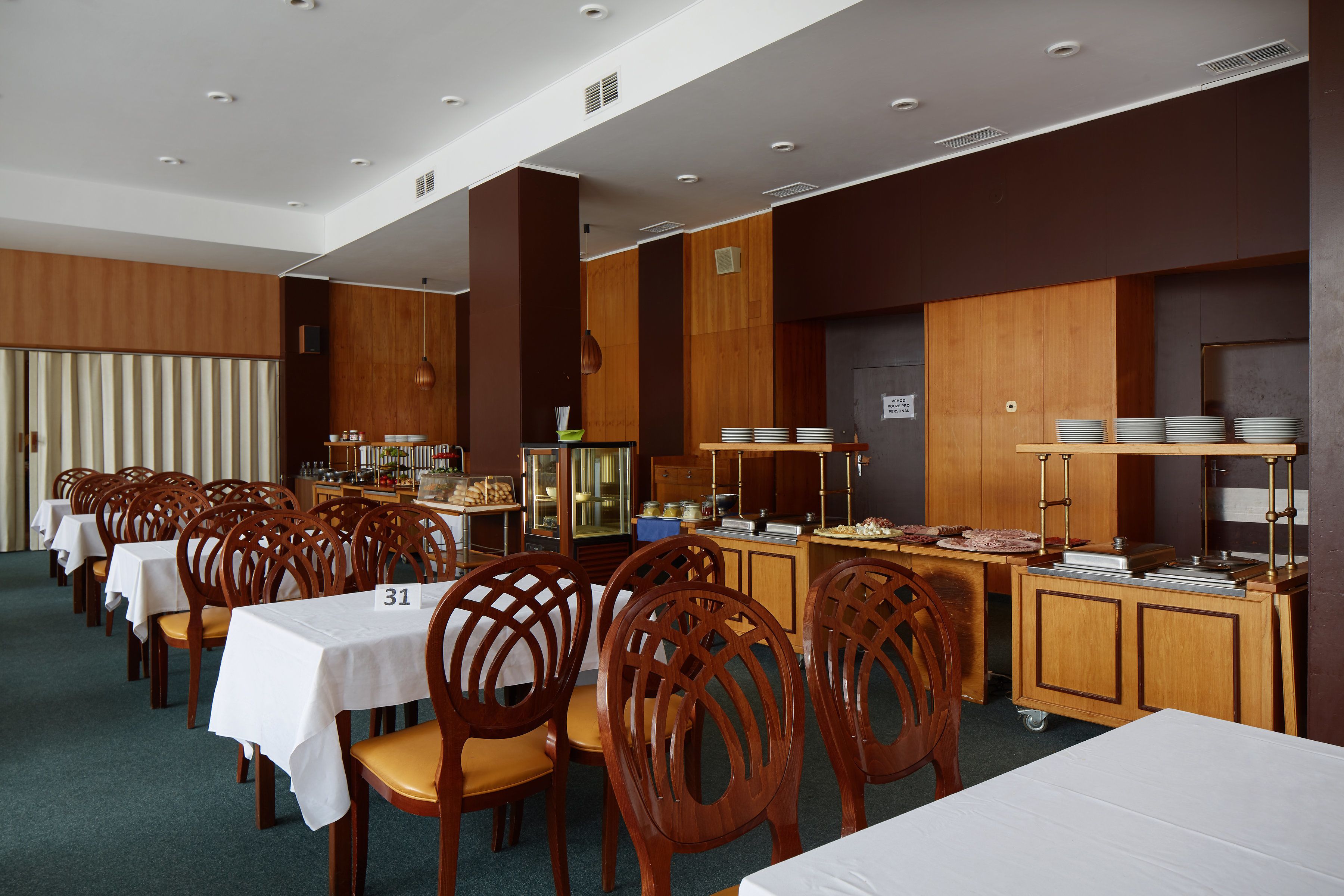 A dining area with multiple tables and chairs, a buffet station, and a kitchen area.