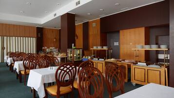 A dining area with multiple tables and chairs, a buffet station, and a kitchen area.