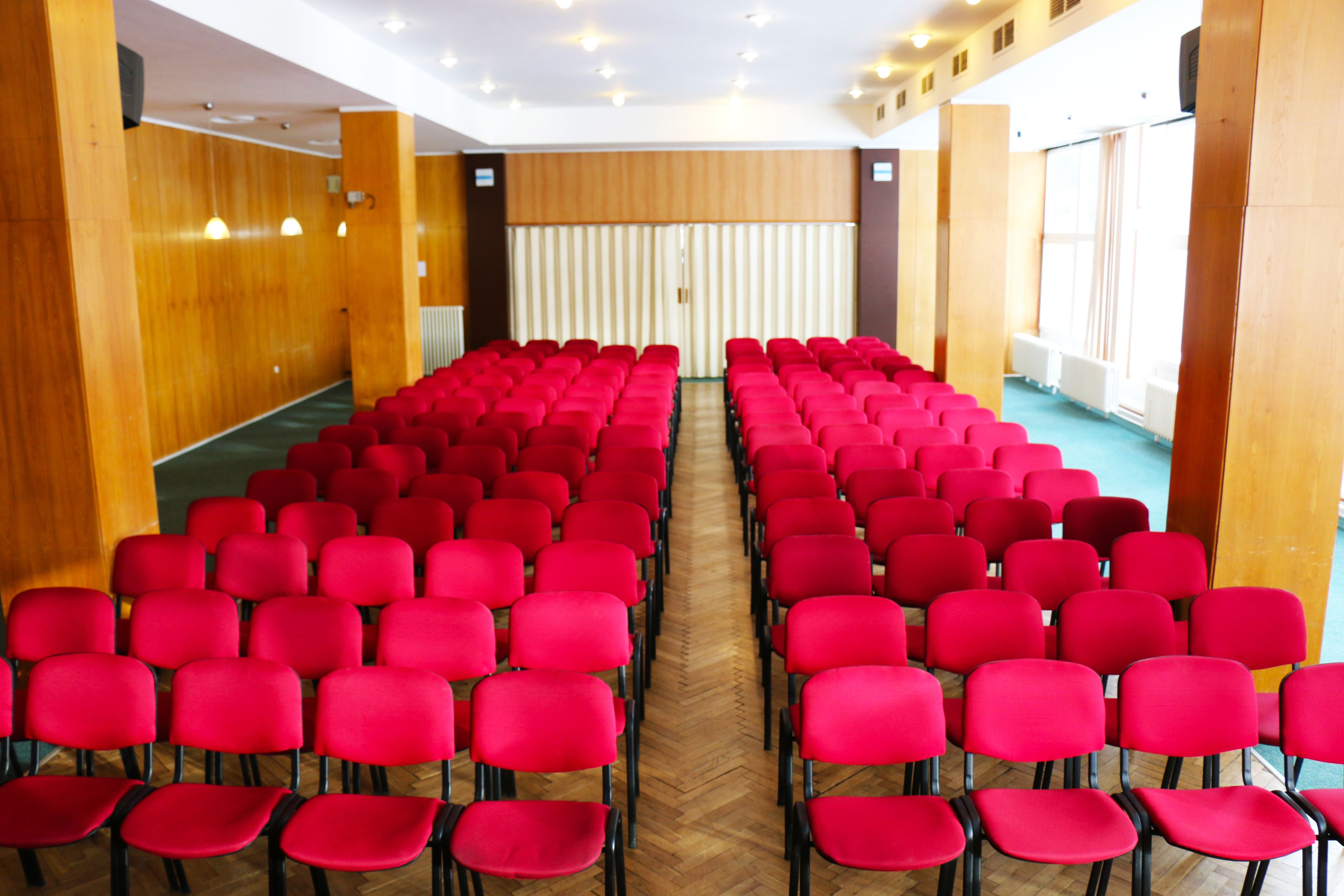 A conference room with rows of red chairs, wooden panel walls, and large windows.