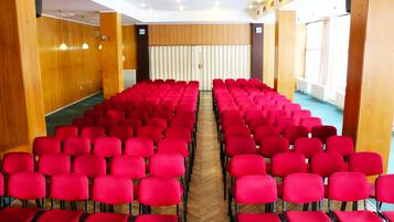 A conference room with rows of red chairs, wooden panel walls, and large windows.