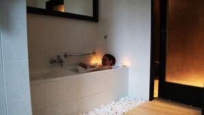A bathtub with a wooden floor and white tiles, a towel rack, and a candle. - Hotel Medlov (Frysava pod Zakovou horou)