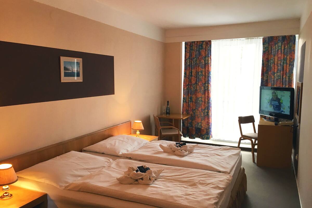 A hotel room with two beds, a desk with a chair, a television, and a window with curtains.
