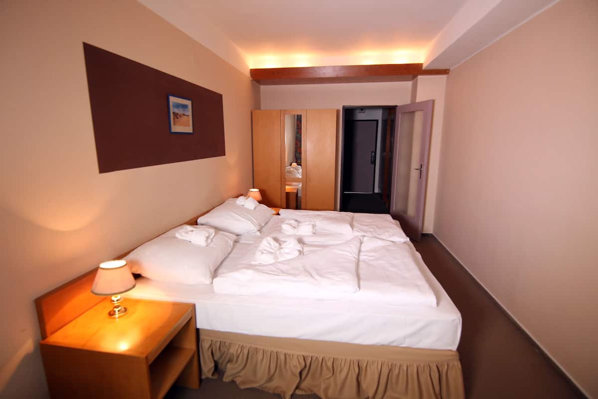A hotel room with a neatly made bed, a bedside lamp, and a door leading to another room.