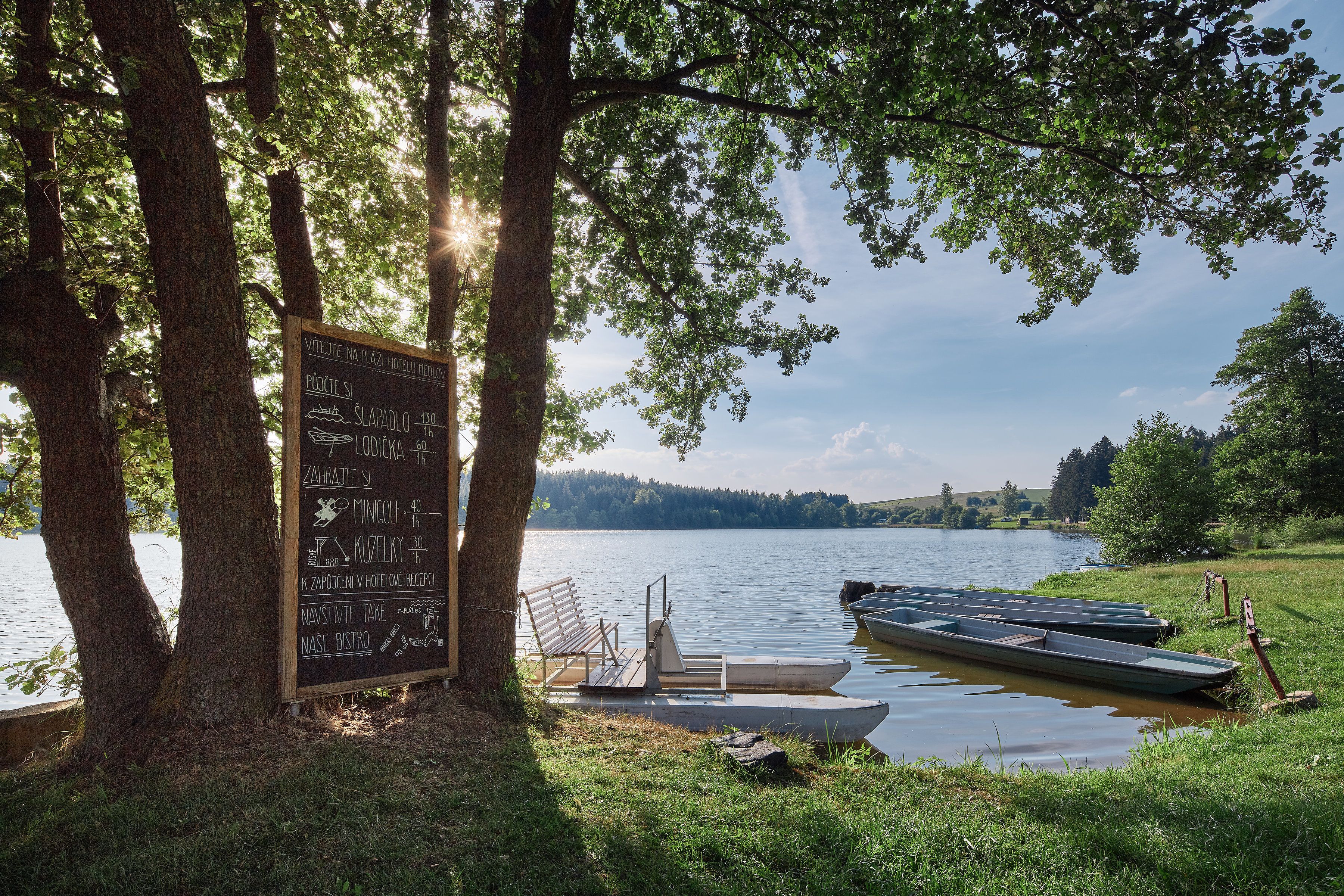 A lakeside view with a signboard listing amenities such as a restaurant, bar, and boat rental services.