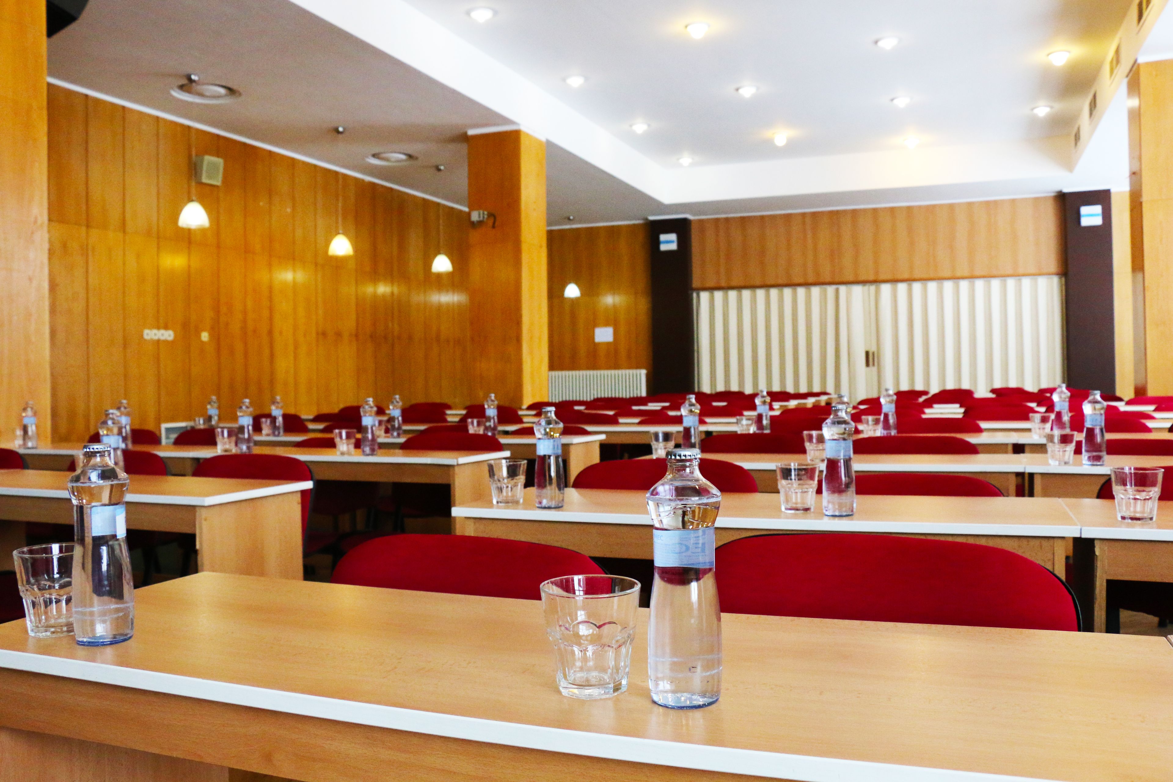 Uma sala de conferências com paredes de madeira, cadeiras vermelhas e mesas organizadas para reuniões.