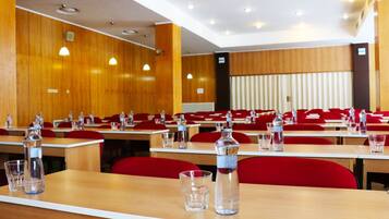 Uma sala de conferências com paredes de madeira, cadeiras vermelhas e mesas organizadas para reuniões.