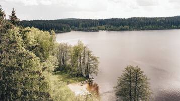 Un lago rodeado de un bosque tupido, una playa de arena y un muelle con un bote.
